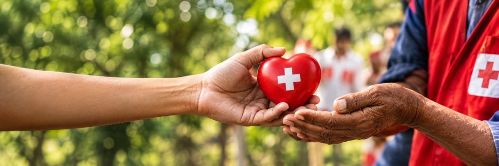 A donor passing a red heart with a white cross into a volunteer’s hands